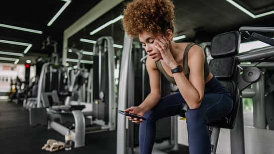 Junge Frau macht eine Pause im Fitnessstudio und schaut auf ihr Smartphone