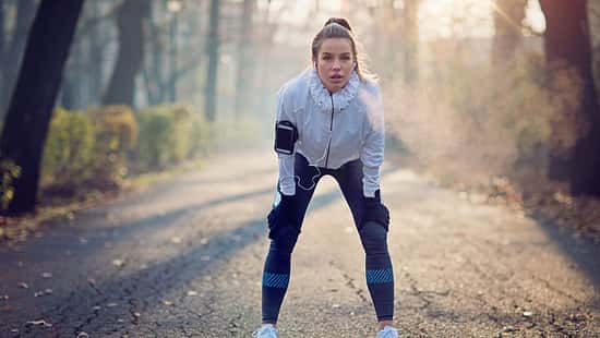 Eine Frau in Laufkleidung steht erschöpft in einer Baumallee.