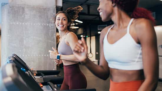 Zwei Sportlerinnen trainieren auf einem Laufband im Fitnessstudio