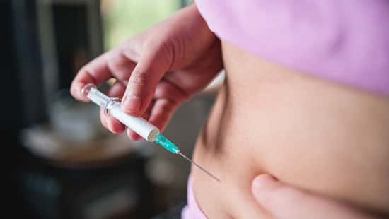 Eine Frau steckt sich eine Spritze in den Bauch