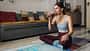 Millennial woman drinks a milkshake while sitting on an exercise mat in the living room