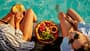 Zwei Frauen sitzen am Pool und essen einen Obstteller Zwei Frauen sitzen am Pool und essen einen Obstteller