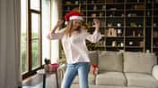 Junge Frau mit Weihnachtsmütze tanzt fröhlich vor dem Tannenbaum