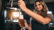 Young,Woman,Dispensing,Beer,In,A,Bar,From,Metal,Spigots.
