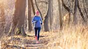Joggerin läuft in langem Sportoutfit durch einen herbstlichen Wald