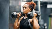 Eine durchtraininerte Frau traininert mit zwei Hanteln in einem Fitnessstudio.