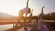 group of women exercising yoga on jetty in the city at sunrise