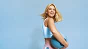 hübsche blonde junge frau mit medizinball unterm Arm vor hellblauen Hintergrund