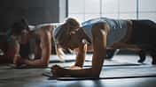 mehrere Frauen führen auf Yogamatten den Unterarmstütz aus