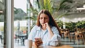 Frau sitzt mit Handy in einem Café und sieht traurig aus