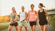vier fröhliche und fitte Frauen gehen in Sportkleidung einen Weg entlang