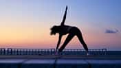 Eine Frau macht eine Yoga-Pose vor dem Sonnenaufgang