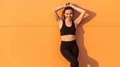 Sportliche junge Frau posiert in Sportkleidung vor orangefarbener Wand