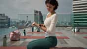 Eine Frau macht Yoga auf einer Dachterrasse und bedient gerade ihre Smartwatch