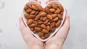 Female hands holding heart shaped plate with peeled almond nuts on light background.Macro.