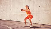 Athletic,Adult,Woman,Doing,Squat,Exercise,Outdoors,Against,Concrete,Wall