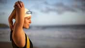 Eine Schwimmerin im Badeanzug stretcht sich am Strand