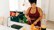 Frau in Sportkleidung bereitet Smoothie zu und schneidet Obst