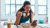 Junge Frau isst einen Salat und schaut auf ihr Handy