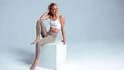 Smiling fitness model sitting on white cube in studio