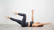 Woman performing dead bug exercise lowering opposite arm and leg for functional core training