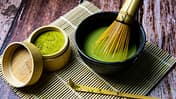 Matcha-Pulver und Matcha-Tee in einer Schale mit Bambusbesen auf einer Bambusmatte.