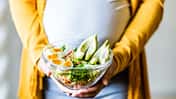 Eine schwangere Frau hält eine Salatschüssel vor dem Bauch Eine schwangere Frau hält eine Salatschüssel vor dem Bauch