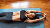 Eine Frau liegt mit geschlossenen Augen auf einer Yogamatte und macht hypopressive Bauchmuskelübungen