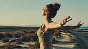 Young pretty woman standing outdoors enjoy moment of freedom with outstretched arms feel happy and satisfied, sea and coastline on background. Life, moments concept