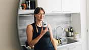 Smiling Woman Reflected in Mirror In Modern Kitchen Holding A Coffee Mug With A Smile On It