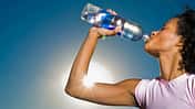 Eine Frau trinkt aus einer Plastikflasche, während im Hintergrund die Sonne scheint
