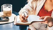 Eine Frau sitzt in einem Cafe an einem Tisch und schreibt in ihr Journal