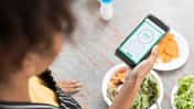 Frau checkt während dem Essen ihre Intervallfasten-App auf dem Smartphone