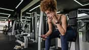 Junge Frau macht eine Pause im Fitnessstudio und schaut auf ihr Smartphone Junge Frau macht eine Pause im Fitnessstudio und schaut auf ihr Smartphone