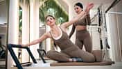 Eine Pilates-Trainerin unterstützt eine Frau beim Pilates-Training auf einer Reformer-Maschine