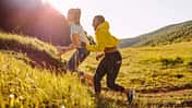 Zwei Freuen joggen durch eine hügelige Landschaft und werden von der Abendsonne angeschienen