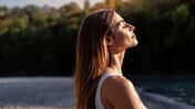 Eine Frau blickt mit geschlossenen Augen in Richtung Himmel. Die Sonne scheint auf ihr Gesicht