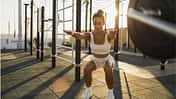 Eine junge Frau macht beim Sonnenuntergang Squats in einer Outdoor Sportanlage.