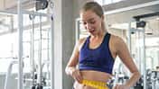 Junge Frau im Fitnessstudio misst ihren Bauchumfang